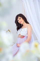 Obraz na płótnie Canvas Gentle pregnancy. Beautiful pregnant in light white dress with orchids