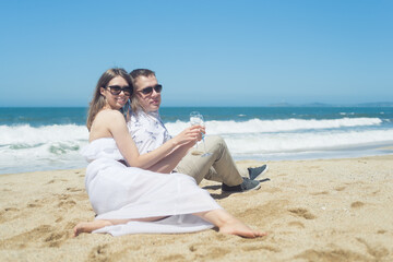 Young romantic couple sitting on the beach drinking champaign