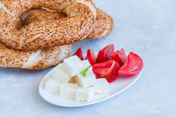 Traditional Turkish bagel (bread) - simit with tomatoes and feta cheese on a plate on a white stone background. Copy space and close up.