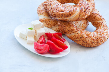 Traditional Turkish bagel (bread) - simit with tomatoes and feta cheese on a plate on a white stone background. Copy space and close up.