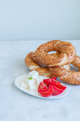 Traditional Turkish bagel (bread) - simit with tomatoes and feta cheese on a plate on a white stone background. Copy space and close up.