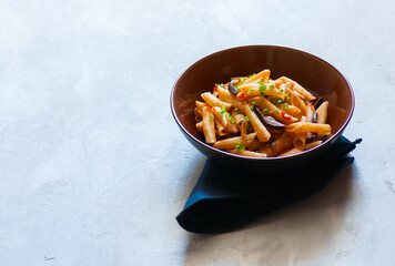 Close up of italian penne pasta with eggplants and tomato sauce in a brown bowl on a white stone background. Copy space and overhead view. Traditional food concept.