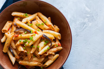 Close up of italian penne pasta with eggplants and tomato sauce in a brown bowl on a white stone background. Copy space and overhead view. Traditional food concept.