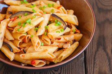 Close up of italian penne pasta with eggplants and tomato sauce in a brown bowl on a white background. Copy space and overhead view. Traditional food concept.