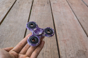 A hand holding fidget spinner purple colour stress relieving toy on wooden background.