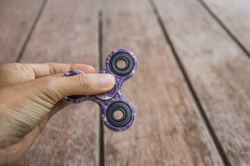 A hand holding fidget spinner purple colour stress relieving toy on wooden background.