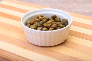 bowl with fresh capers on wooden table