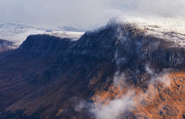A snow and cloud covered summit of Beinn A Mhuinidh above Loch Maree in the Scottish Highlands, Scotland, UK.