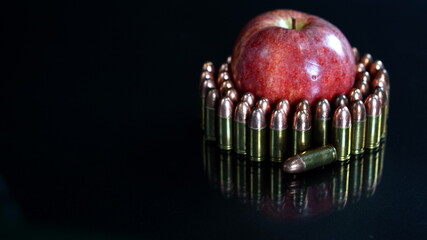 Bullets and a red apple bill on the black mirror floor. Bullets are a projectile expelled from the...