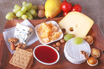 Assortment of cheese with fruits, grapes and nuts on a wooden serving tray.