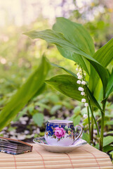 A small Cup of tea next to the flowers of lilies of the valley