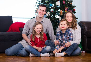 young parents and children posing for photo by Christmas tree