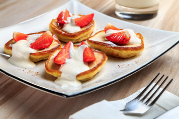 pancakes with strawberries and sour cream on a beautiful plate stand on the table