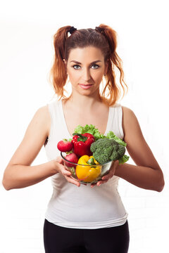 Redheaded caucasian girl holding glasses bowl with fres sweet peppers, radish, broccoli and lettuce
