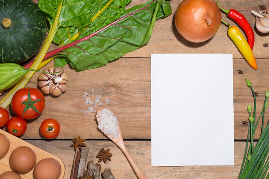 Open recipe book with fresh vegetables on wooden table.