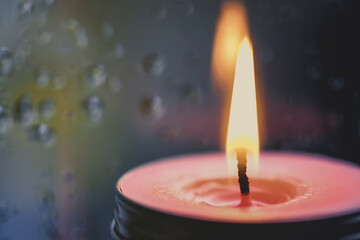 Vintage image of Light of Pink Candle in the front at window with blurred rain drops and low light nature background