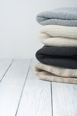 Knitted wool sweaters. Pile of knitted winter clothes on wooden background, sweaters, knitwear, space for text.