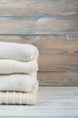 Knitted wool sweaters. Pile of knitted winter clothes on wooden background, sweaters, knitwear, space for text.