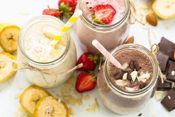 Banana chocolate and strawberry milkshakes in jars on white.