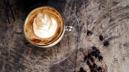 Hot cappuccino with streamed milk. Pour the hot latte art by milk. A cup of coffee put on the wood table with shiny dark roasted Italian coffee beans. Aroma and flavor beverage.