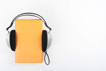 Audiobook on white background. Headphones put over yellow hardback book, empty cover, copy space for ad text. Distance education, e-learning concept.