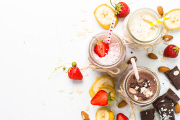Banana chocolate and strawberry milkshakes in jars on white. Top view.
