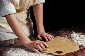 The girl in an apron cuts dough shaped cookies in the form of stars on a wooden table. Close-up.