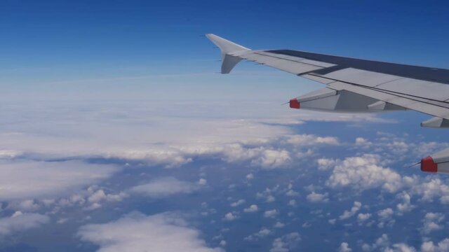 View from a plane window: a plane wing over clouds and blue sky. Traveling by air. Airplane flying above earth at 10000 m -50 °C  (-58.0 °F). Ice and dust on airplane window. 4K footage at 60fps.