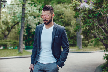 Fototapeta premium Stylish man with a beard and in sunglasses standing in the park.