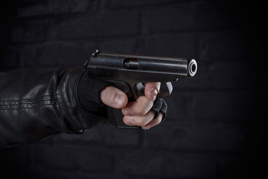 Gangster with a gun in his hand and a leather jacket on a dark background