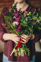 A girl in a burgundy blouse holds a bouquet of tulips, boxwood and plants with a manicure