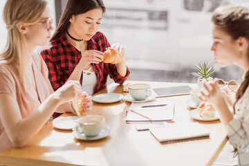 young girls eating croissants and drinking coffee at cafe, coffee break