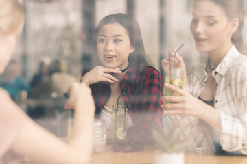 young girls drinking cocktails together while sitting at table in cafe, having lunch