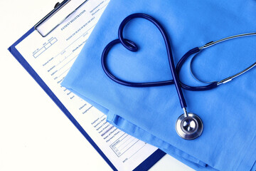 Medical stethoscope twisted in heart shape lying on patient medical history list and blue doctor uniform closeup