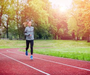 Obraz premium Athletic woman running on track with smart phone app, fitness lifestyle