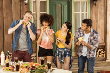 young multiethnic friends eating burgers at picnic on patio
