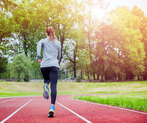 Obraz premium Athletic woman running on track back view, healthy lifestyle