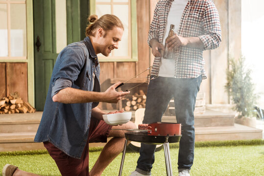 Two Men Grilling Burgers While Drinking Beer Together Outdoors