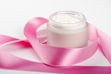 Bottle of cream for face next to pink ribbon on white background.