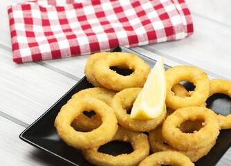 Close-up of a plate of squid a la romana, a lemon on a black plate. Squids.Horizontall shoot.