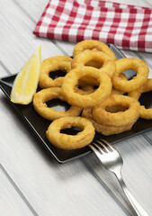 Close-up of a plate of squid a la romana, a lemon on a black plate. Squids. Vertical shoot.