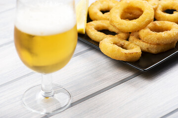 Beer glass next to squids a la romana on wooden board.