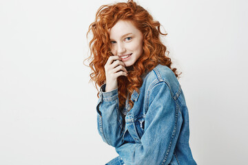 Pretty shy ginger girl smiling looking at camera over white background. Copy space.