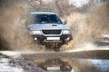 Fototapeta na wymiar Japanese SUV on dirt road in early spring making splashes from a puddle