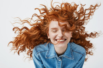 Attractive cheerful redhead girl with flying curly hair smiling laughing with closed eyes over white background.