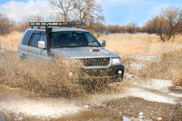 Fototapeta na wymiar SUV on dirt road in early spring making splashes from a puddle