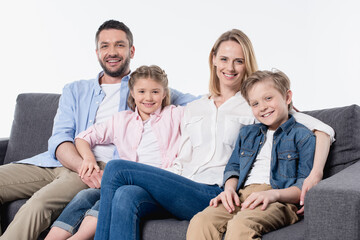 Happy family with two children sitting together on couch and smiling at camera