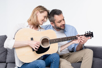 Happy young couple sitting together on sofa and playing guitar isolated on white