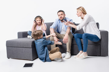 caucasian family sitting on sofa with digital devices isolated on white