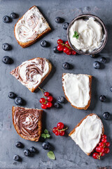 Variety of dessert sandwiches with berries and cream cheese and chocolate swirl. Red currant, blueberries, sliced kiwi, figs over gray metal background. Flat lay, summer appetizer concept